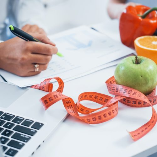 Female nutritionist in white coat sitting indoors in the office at workplace.